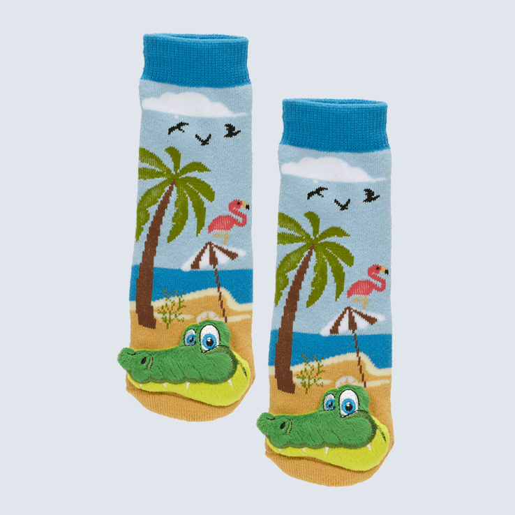 Two blue socks against a white background. The socks show a beach scene with a palm tree, flamingo, beach umbrella, and bird motifs. Each socks has an alligator charm on each toe.