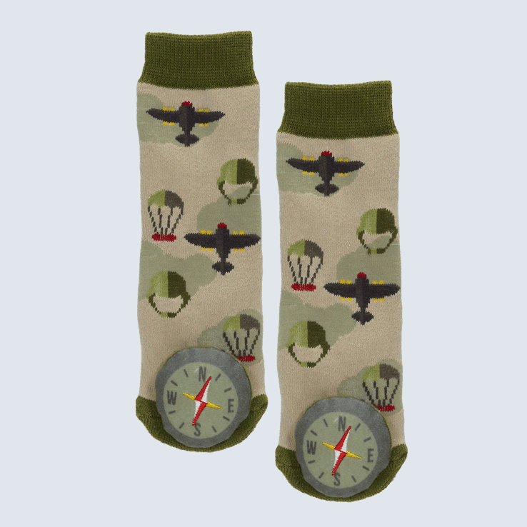 Two green and brown socks against a white background. The socks feature plane and parachute motifs and a plush compass charm on each toe.