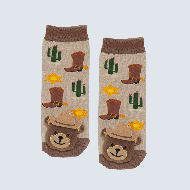 Two socks against a white background. The socks feature cowboy boot and cactus motifs with a cute plush bear charm on the toe.